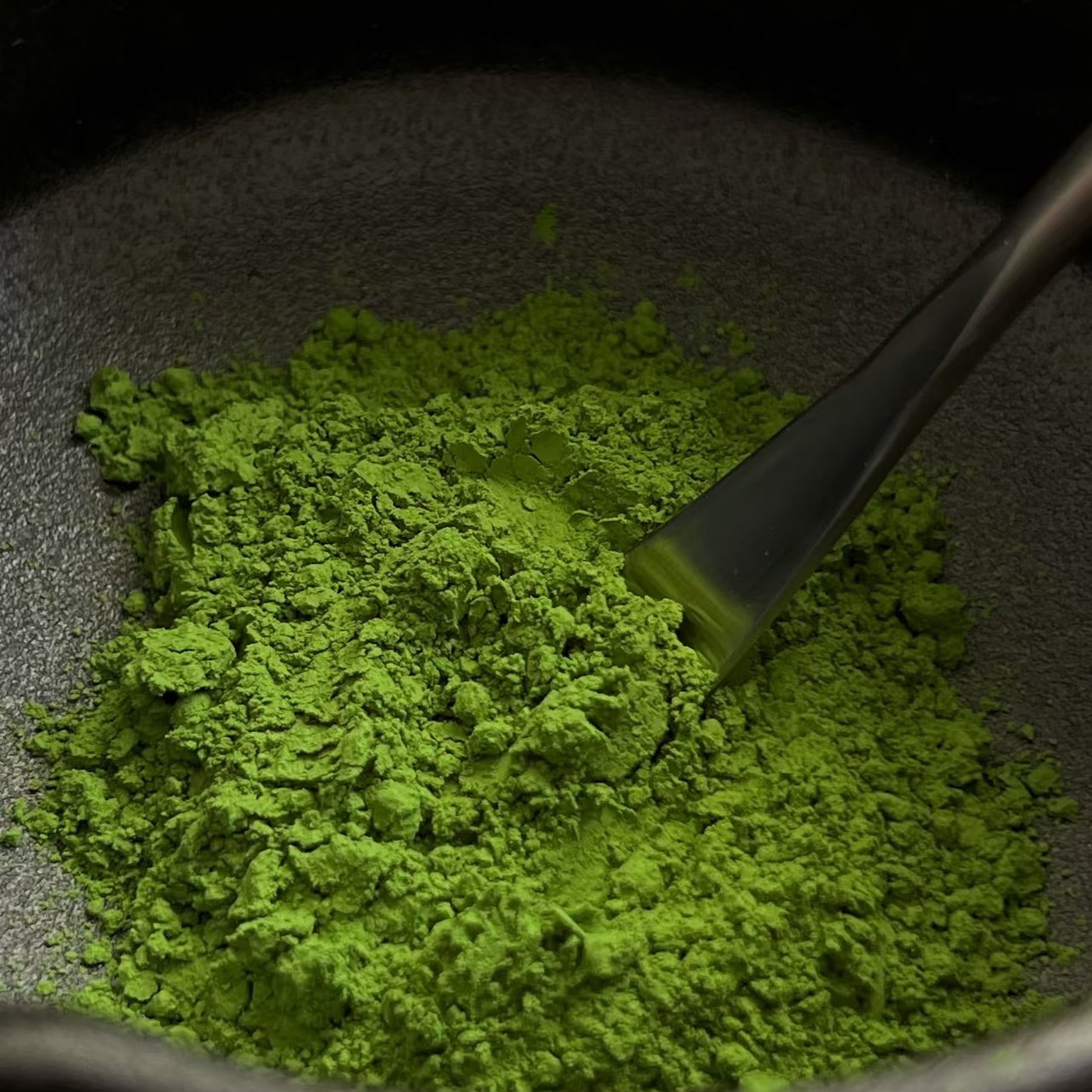 Poudre de matcha vert vif tamisée dans un bol avec une cuillère chashaku
