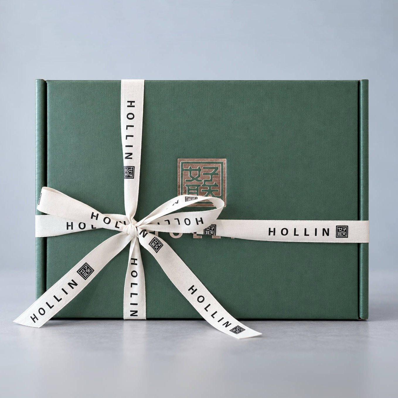 Coffret cadeau vert HOLLIN noué de son ruban signature crème, fermé du sceau cuivre de la maison.